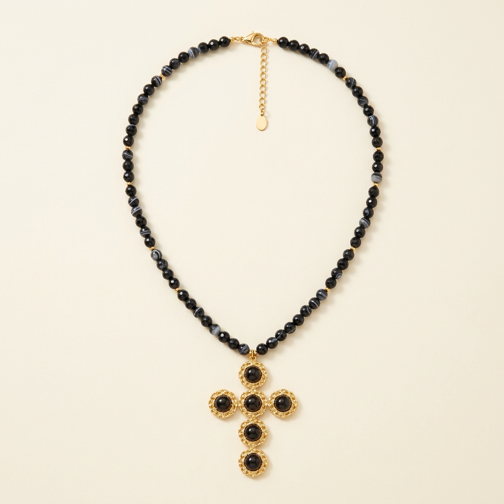 Collana Croce Noir con perline nere e croce color oro su fondo avorio
