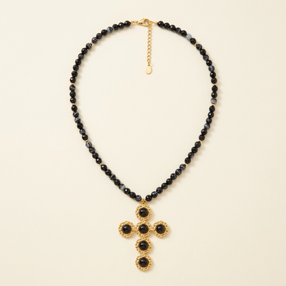 Collana Croce Noir con perline nere e croce color oro su fondo avorio