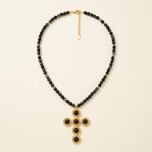 Collana Croce Noir con perline nere e croce color oro su fondo avorio