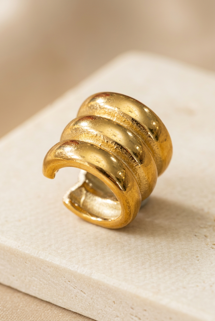 Ear Cuff Maly in acciaio dorato a tre fasce appoggiato su fondo avorio