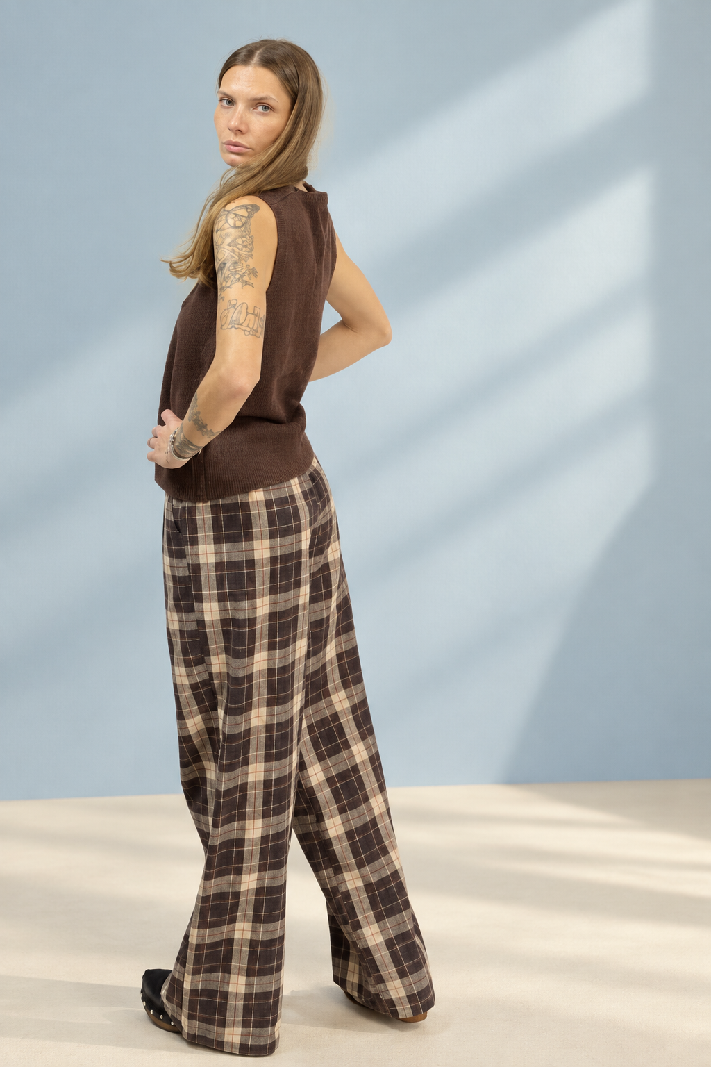Pantalone Checks a quadri marroni e crema, vista laterale su sfondo azzurro polvere