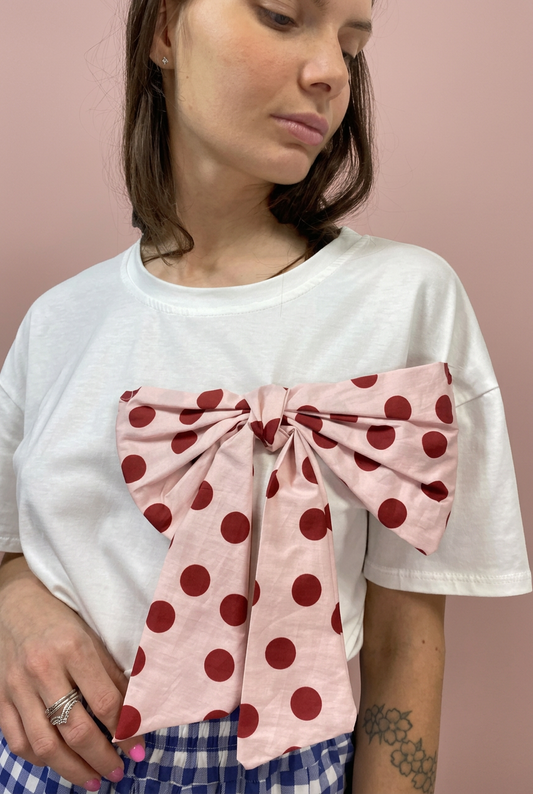 T-shirt bianca con grande fiocco rosa a pois bordeaux su sfondo rosa cipria
