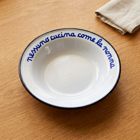 Piatto bianco con scritta blu Nessuno cucina come la nonna su tavolo in rovere color miele