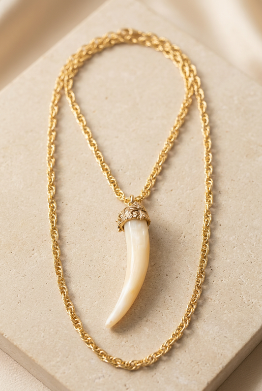 Collana dorata con pendente a corno color avorio appoggiata su fondo chiaro